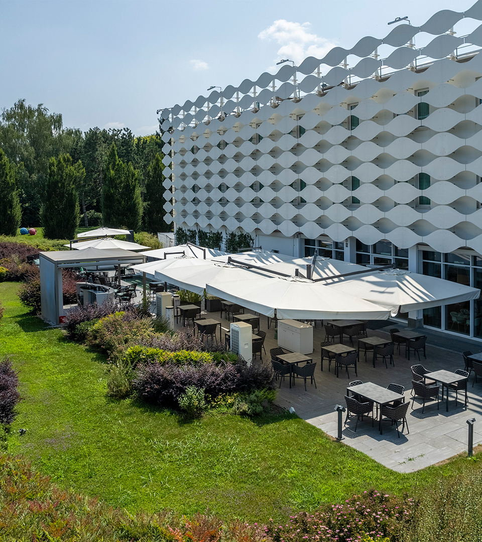 Lounge Bar esterno con tavoli sotto grandi ombrelloni bianchi immerso nel verde