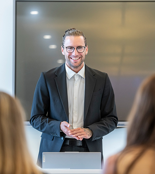 Relatore sorridente in giacca durante una presentazione in sala meeting
