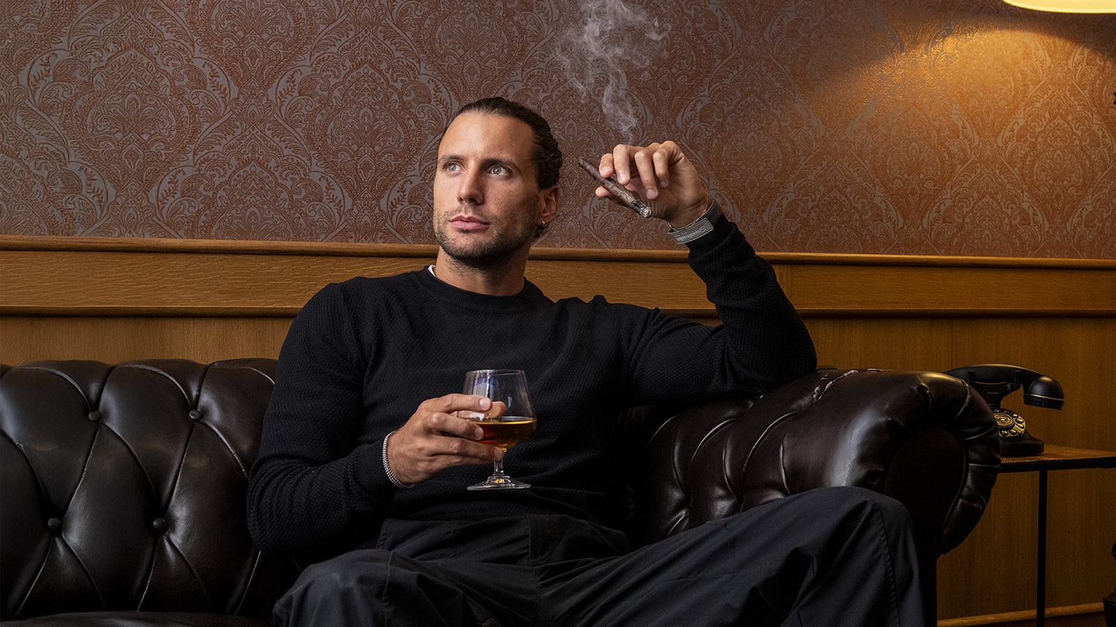 Ospite rilassato nella cigar room con sigaro acceso e bicchiere di distillato