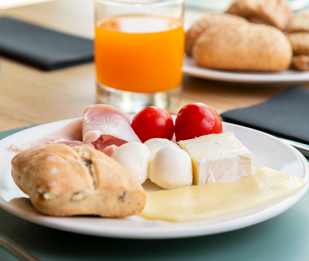 Colazione salata con un piatto di formaggi, affettati, mozzarelline, pomodori e pane fresco