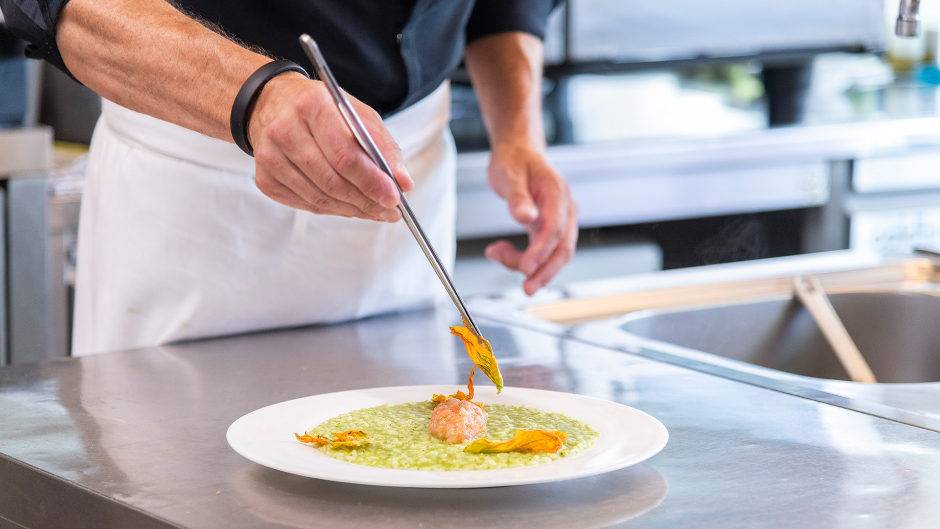 Le mani dello chef mentre guarniscono con precisione un risotto con fiori di zucca nella cucina del Bloom Restaurant