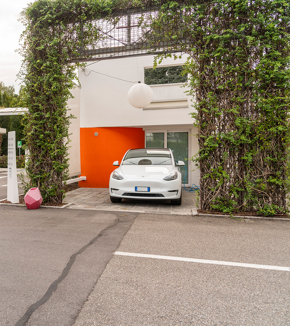 Parcheggio privato di fronte all'ingresso di una camera del MOOM Hotel, con un'auto elettrica in carica