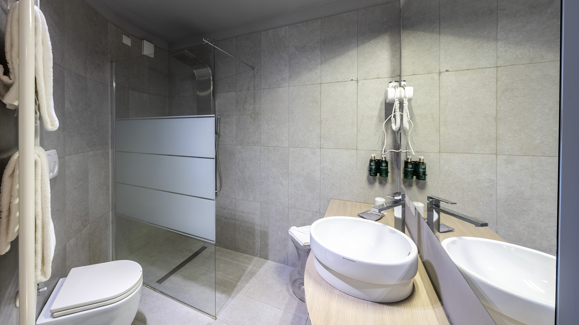 Bagno Camera Deluxe con ampia doccia walk-in in vetro satinato, lavabo rotondo su piano in legno, grande specchio a parete, asciugamani bianchi e set cortesia
