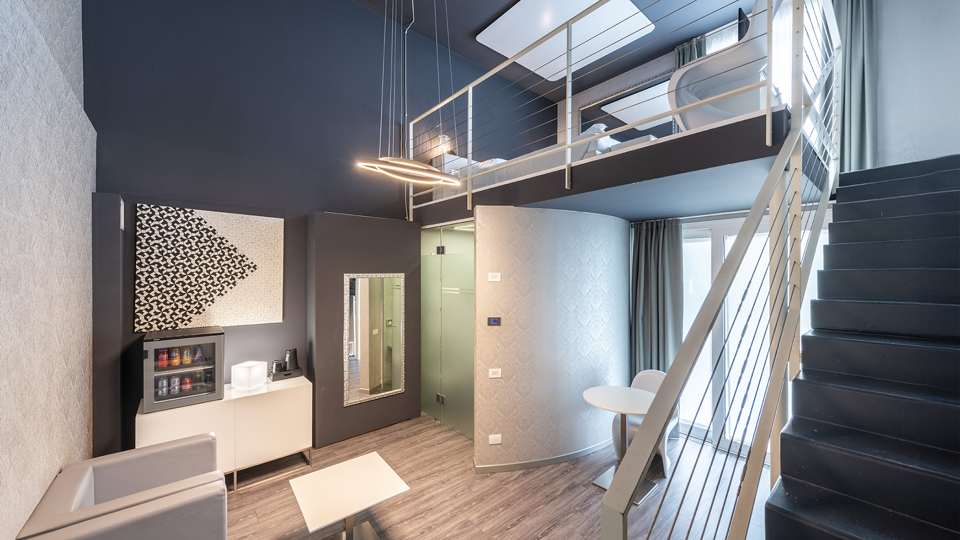 Suite moderna con pareti grigio scuro, luci soffuse, scala interna con ringhiera e ampie finestre